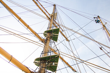 A towering ship mast seen from below, adorned with intricate ropes and rigging elements.
