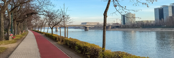A serene riverbank path in an urban European setting under a clear winter sky, ideal for relaxation and urban planning themes
