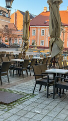 Empty outdoor cafe seating with closed umbrellas on a cobblestone street, symbolizing urban isolation during off-peak hours, Europe