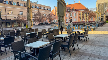 An empty outdoor cafe in a European city square captures urban solitude and the impact of seasonal weather changes