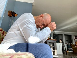 Bald senior citizen worried emotion with his head down on his hands.