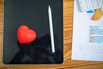 Red heart symbol placed on screen glass of tablet placed on the desk and the heart symbolizes love...