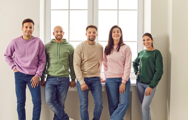 Fototapeta premium A group of smiling friends in jeans and a sweatshirt are standing in a room by the window. Portrait of smiling young people in casual clothes. Team in an empty room. Maintain friendship