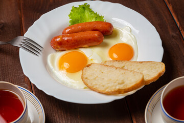 Breakfast fried eggs with sausages, crispy white bread and greens, and tea on the table