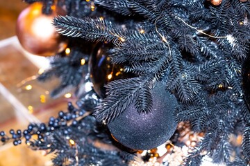 Black shiny holiday decorations on a Christmas tree against a bokeh background of Christmas lights. New Year, Christmas background, glitter.