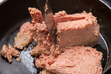 Frozen ground beef in a frying pan with vegetable oil is broken up with a spatula