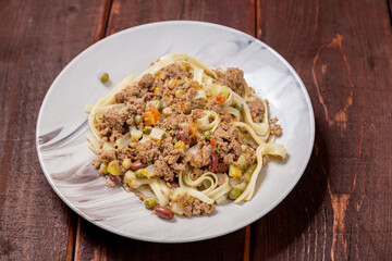 Noodles with minced meat and vegetables in sauce in a plate on the table close-up