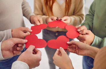 Close up view of the hands of a diverse group of volunteers standing in a circle, each holding a...