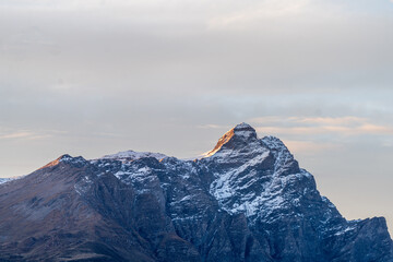 mountain peak snow cap partially illuminated at sunset. detail of cliff. soft rose colored cloudy sky. close up