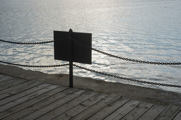 silhouette of sign, barrier chain fence, and wooden pier on the lake, foggy weather, mild December