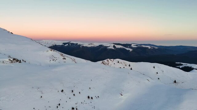Aerial ascending drone view of mountains landscape at sunset in the winter season. Hills covered by snow in Bucegi natural park, Romania