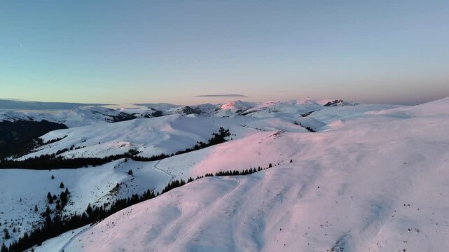 Aerial ascending drone view of mountains landscape at sunset in the winter season. Hills covered by snow in Bucegi natural park, Romania