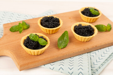 Tartlets with black caviar served on on wooden table