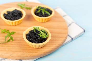 Tartlets with black caviar served on on wooden table