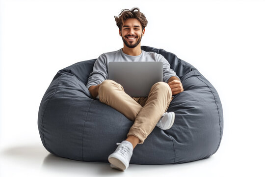 A man is sitting on a bean bag chair and using a laptop. He is smiling and he is enjoying himself. Concept of relaxation and leisure