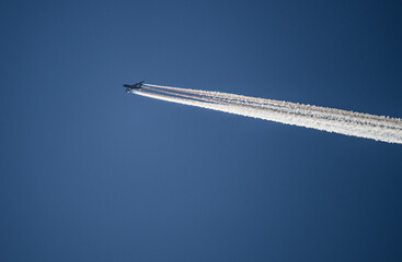 Jet soaring high above clear blue sky, leaving behind distinct contrails during daytime flight