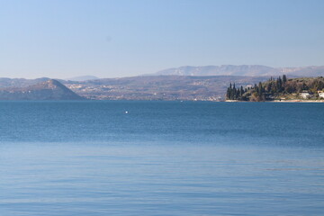 Calm lake garda waters reflecting the blue sky with rocca di manerba and cypress trees