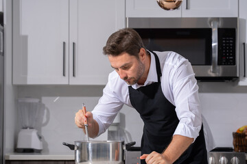 modern chef in professional uniform. close-up on the hand of male chef who is stirring soup in pot...