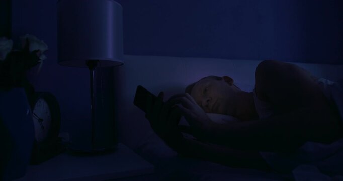 Man wake up in middle night and scrolling feed on mobile phone app lying in bed, Internet addiction concept and doom scrolling
