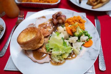 Roast turkey Christmas dinner with vegetables, gravy and a Yorkshire pudding. There are also sausages wrapped in bacon.