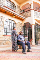 A middle-aged woman giving her partner a hair trim ah home on a warm sunny morning 