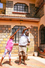 An older African couple doing stretches and workout outdoors while at home.