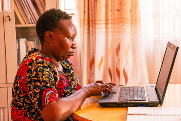 A middle-aged African woman working remotely on her laptop at home