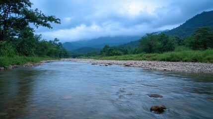 Serene riverbank landscape post-rainfall showcasing tranquil water amidst lush greenery and distant mountains under a cloudy sky