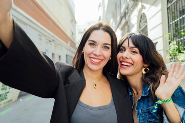 Two happy women taking selfie and waving in the street