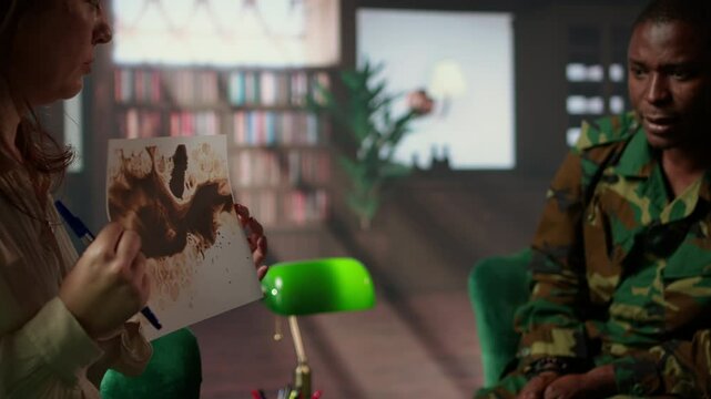 Military veteran studies Rorschach inkblot in therapy session with counselor, addressing PTSD and trauma recovery problems. Woman shows psychological support for mental health care. Camera A.