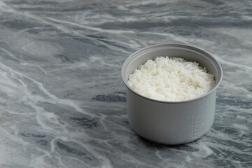 Cooked rice in a rice cooker pan. Concept of food sources of carbohydrates. Clean white cooked rice.Marble table background.Copy space for text.For graphic design or banner background