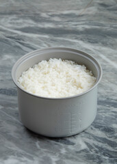 Cooked rice in a rice cooker pan. Concept of food sources of carbohydrates. Clean white cooked rice.Marble table background.Copy space for text.For graphic design or banner background