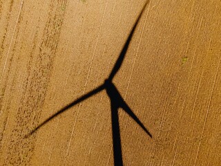 High-angle view of a wind turbine's shadow on a harvested field. Renewable energy source. ,...