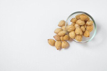 Close up of candlenut seeds spilling from glass cup isolated white background.Natural candlenut tekture background.Copy space for text.Concept of spices.For graphic design or banner background