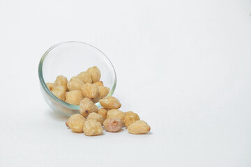 Close up of candlenut seeds spilling from glass cup isolated white background.Natural candlenut tekture background.Copy space for text.Concept of spices.For graphic design or banner background
