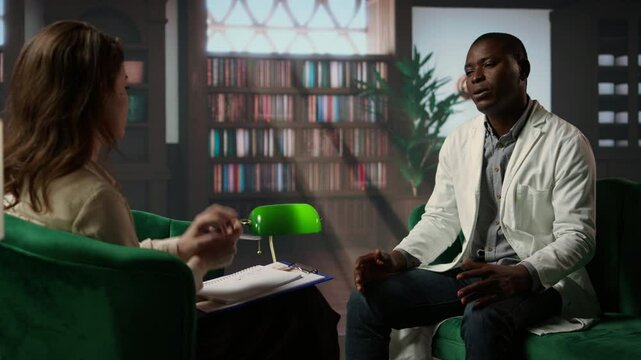 Black medic feeling overworked and deals with anxiety sharing his PTSD feelings at counseling session. Doctor in consultation, receives support against depression and trauma. Camera A.