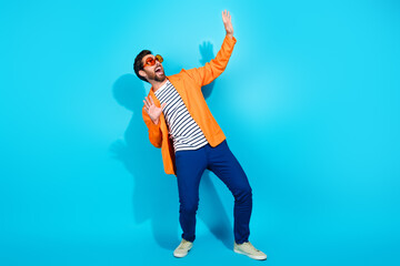 Charismatic young man in vibrant orange jacket posing against turquoise background, expressing joy...