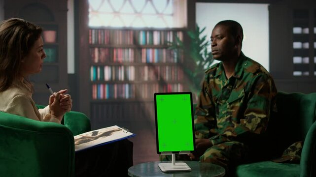 Infantry serviceman attending a therapy session with psychologist next to mockup display, suffering from PTSD after combat. Female counselor offers help and support to army officer. Camera A.