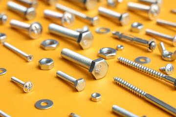 Arrangement of different tap bolts, screws and chrome nuts on orange background