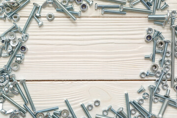 Frame made from tap bolts and chrome nuts on white wooden background