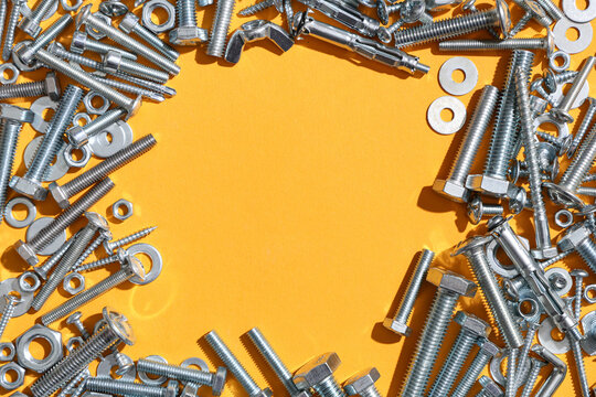 Frame made from different tap bolts, screws and chrome nuts on orange background