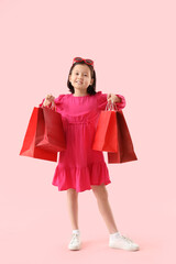 Cute little Asian girl with shopping bags on pink background