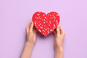 Female hands with red paper heart on lilac background. Valentine's Day celebration