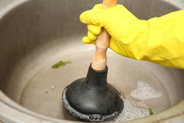 Woman cleaning clogged kitchen sink with plunger, closeup
