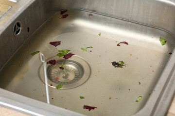 Clogged metallic kitchen sink with water and food leftovers, closeup