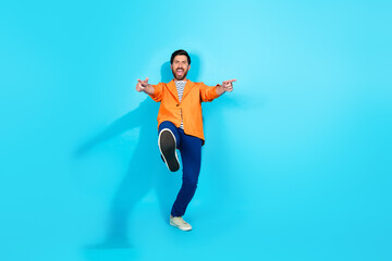Charismatic young man in vibrant orange jacket dances joyfully against a striking teal background