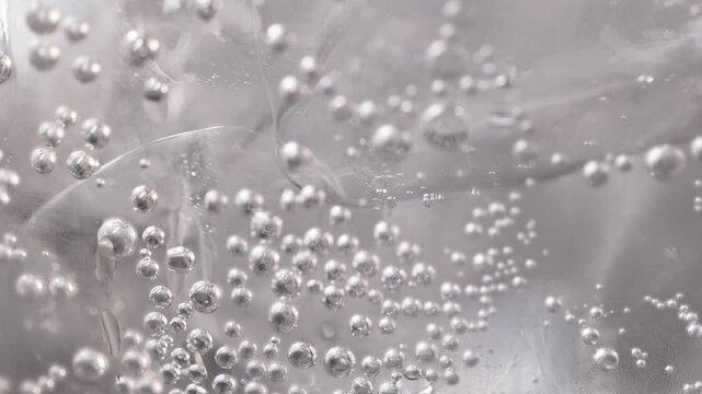 Close-up of a sparkling carbonated drink with bubbles, zoom in macro, neutral color. Soda with ice and bubbles. Sparkling cold soft drink, carbonated liquid and cool iced tonic in a glasses