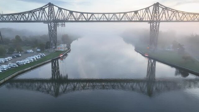 The Rendsburg High Bridge over Kiel Canal with its aerial transfer bridge, while morning mist drifts through landscape. Drone footage of camping caravan area along Kiel Canal. 