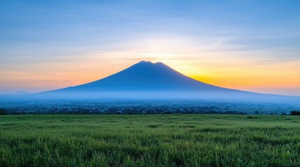 Naklejka premium A stunning sunrise illuminates a majestic volcano, surrounded by lush green fields, creating a breathtaking natural landscape.