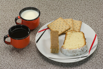 A delightful mix of crackers, pound cake, and a cookie bar served on a plate, accompanied by mugs of hot coffee and fresh milk in vibrant red enamel cups.